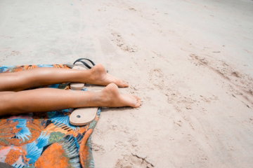 bare foot person lying on orange textile on brown sand during daytime